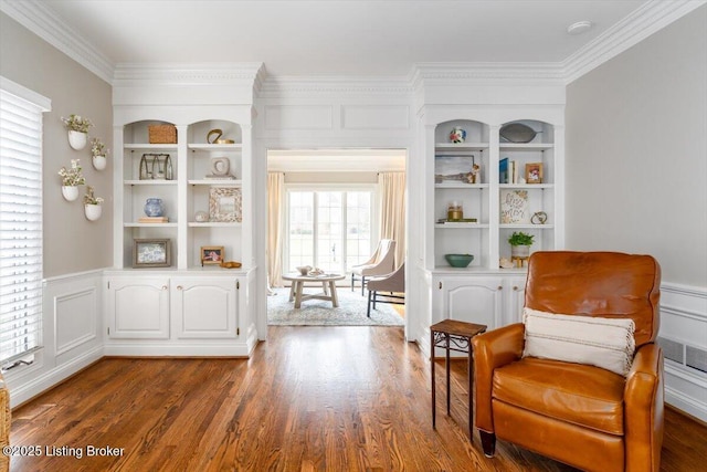 living area with built in features, dark wood-style flooring, a wainscoted wall, and crown molding