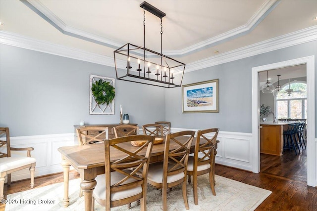 dining room with a wainscoted wall, dark wood-type flooring, a raised ceiling, and crown molding