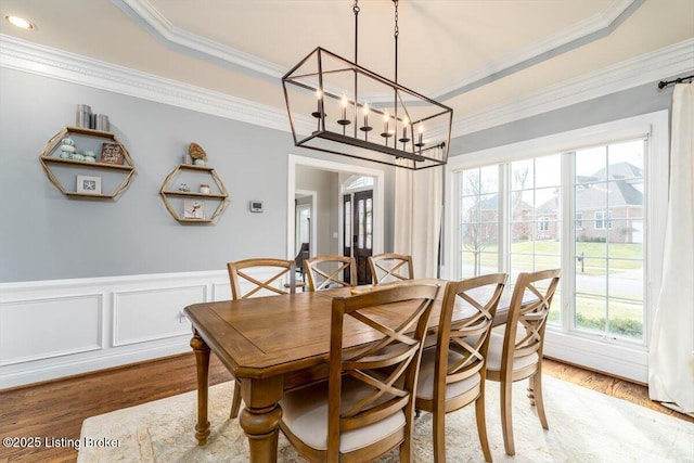 dining area with wainscoting, a raised ceiling, light wood-style flooring, and crown molding