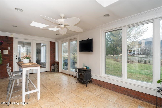 sunroom / solarium with ceiling fan, a wealth of natural light, a skylight, and a wood stove