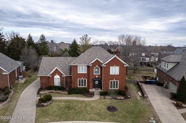 traditional-style home with brick siding, concrete driveway, a chimney, fence, and a front yard