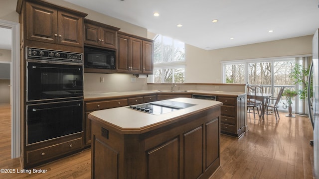 kitchen with wood finished floors, a center island, light countertops, black appliances, and a sink