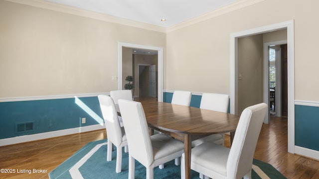 dining space with baseboards, visible vents, ornamental molding, and wood finished floors