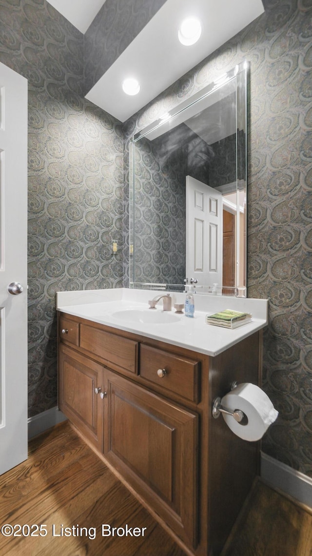 bathroom with wallpapered walls, vanity, baseboards, and wood finished floors