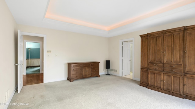 unfurnished bedroom with light carpet, a raised ceiling, and baseboards