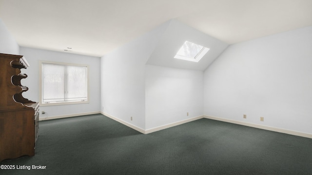 bonus room with dark colored carpet, lofted ceiling with skylight, and baseboards