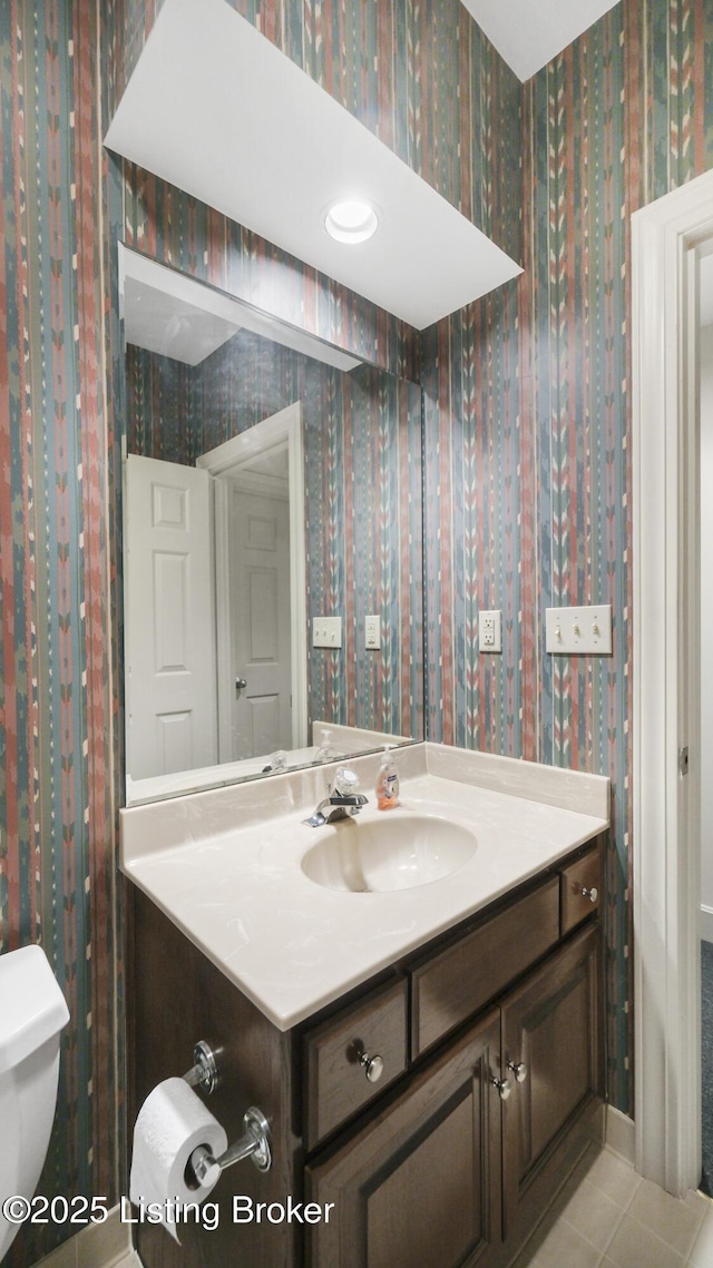 half bath with wallpapered walls, tile patterned floors, and vanity