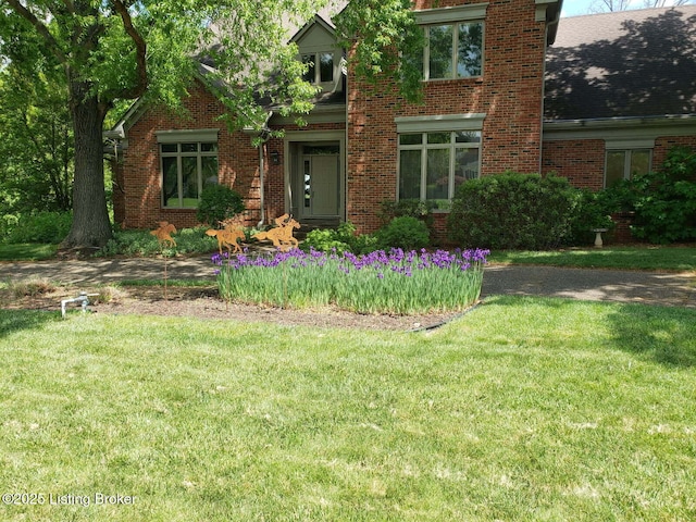 view of front of property featuring a shingled roof, a front yard, and brick siding