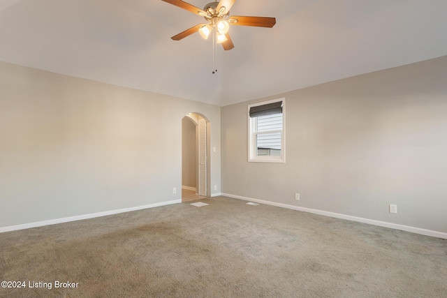 spare room featuring arched walkways, carpet, a ceiling fan, and baseboards