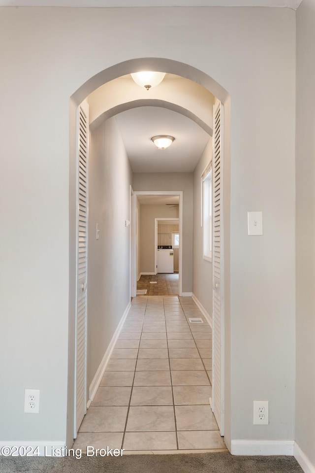 hallway featuring arched walkways, washer / clothes dryer, light tile patterned flooring, and baseboards