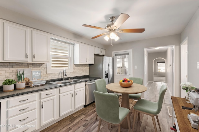 kitchen with decorative backsplash, dark countertops, appliances with stainless steel finishes, white cabinetry, and a sink