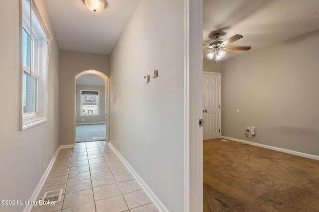 hall featuring light colored carpet, arched walkways, light tile patterned flooring, and baseboards