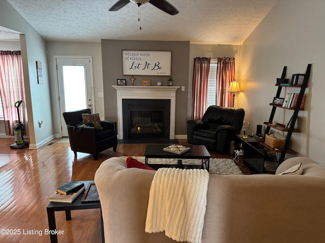 living area featuring a fireplace with flush hearth, a wealth of natural light, wood-type flooring, and a textured ceiling