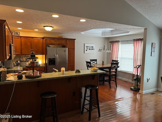 kitchen featuring dark wood-type flooring, a textured ceiling, stainless steel fridge, a peninsula, and a kitchen breakfast bar