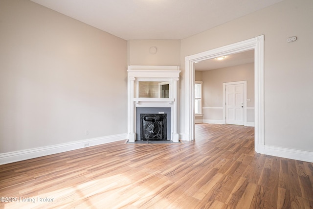 unfurnished living room featuring a fireplace with flush hearth, baseboards, and wood finished floors