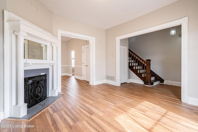 unfurnished living room with stairs, a fireplace, wood finished floors, and visible vents