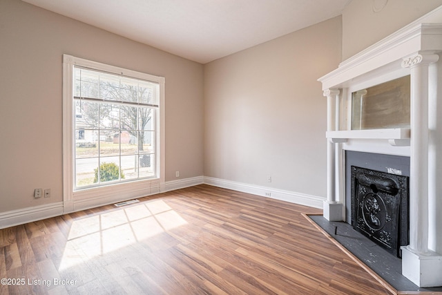 unfurnished living room featuring wood finished floors, a fireplace with flush hearth, and baseboards