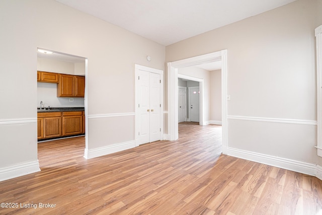 spare room with light wood-style floors, a sink, and baseboards