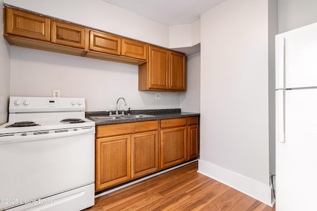 kitchen with white appliances, brown cabinetry, a sink, and light wood finished floors