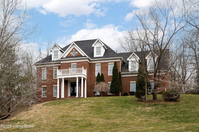 colonial house with brick siding, a front yard, and a balcony