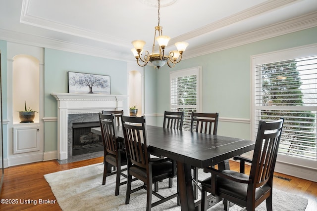 dining space with light wood-type flooring, crown molding, an inviting chandelier, and a premium fireplace