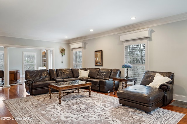 living room featuring decorative columns, crown molding, baseboards, and wood finished floors