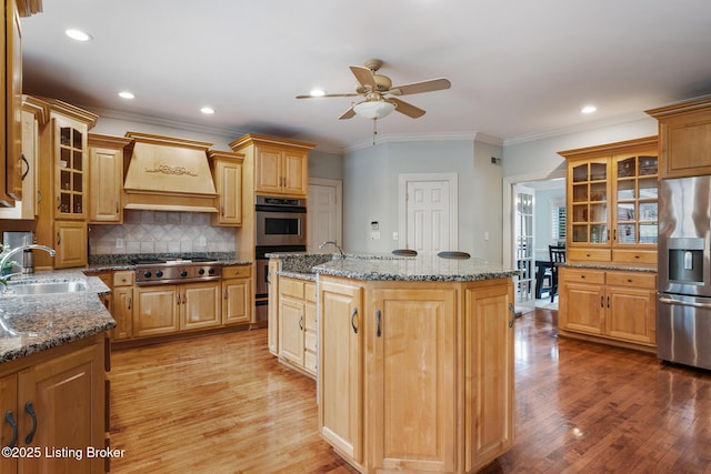 kitchen with custom exhaust hood, stainless steel appliances, light wood-style flooring, a sink, and an island with sink