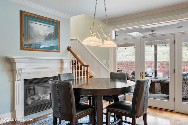 dining room with crown molding, stairway, light wood-style floors, a high end fireplace, and a chandelier