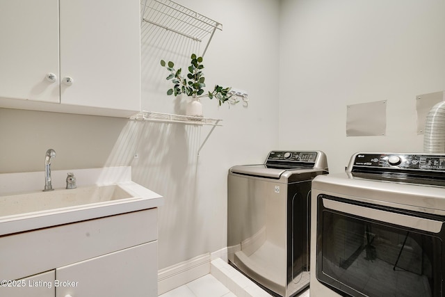 laundry area with cabinet space, light tile patterned floors, baseboards, separate washer and dryer, and a sink