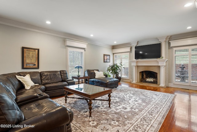 living area with recessed lighting, a fireplace with raised hearth, crown molding, and wood finished floors