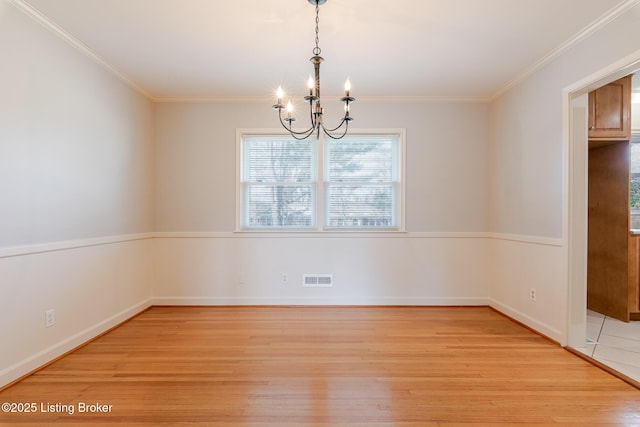 empty room with a notable chandelier, visible vents, baseboards, ornamental molding, and light wood finished floors