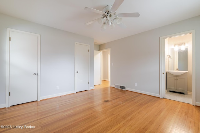 unfurnished bedroom with two closets, visible vents, light wood-style flooring, a sink, and baseboards