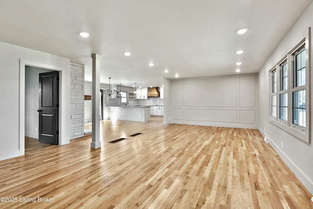 unfurnished living room with light wood-style flooring, decorative columns, a decorative wall, and an inviting chandelier