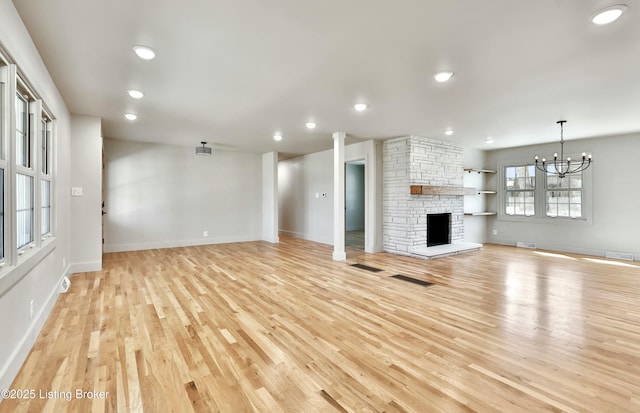 unfurnished living room with a fireplace, visible vents, an inviting chandelier, light wood-style floors, and baseboards