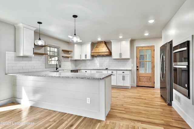 kitchen featuring a peninsula, white cabinets, custom exhaust hood, freestanding refrigerator, and open shelves