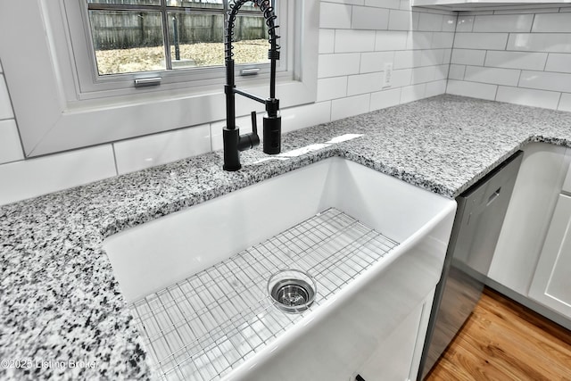 interior details featuring tasteful backsplash, light wood-style floors, a sink, and light stone countertops