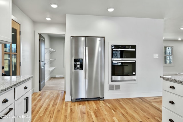 kitchen with light stone counters, visible vents, appliances with stainless steel finishes, light wood-style floors, and white cabinetry