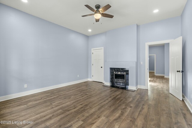 unfurnished living room with dark wood-style floors, ceiling fan, a fireplace, and baseboards