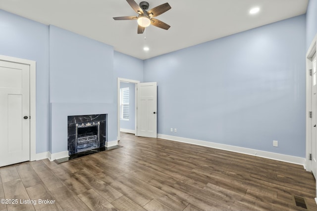 unfurnished living room with recessed lighting, a premium fireplace, a ceiling fan, wood finished floors, and baseboards