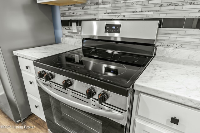 kitchen with electric stove, wood finished floors, white cabinets, and decorative backsplash