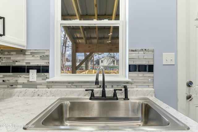 details featuring tasteful backsplash, white cabinets, a sink, and light stone counters