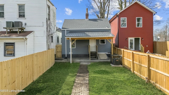 rear view of house with a chimney, a lawn, entry steps, metal roof, and a fenced backyard