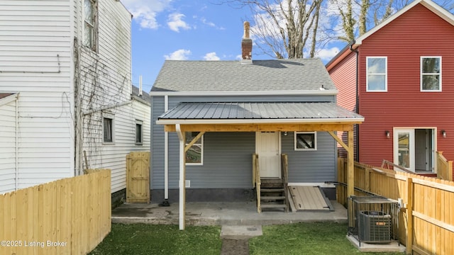 back of property with entry steps, a shingled roof, metal roof, fence, and cooling unit