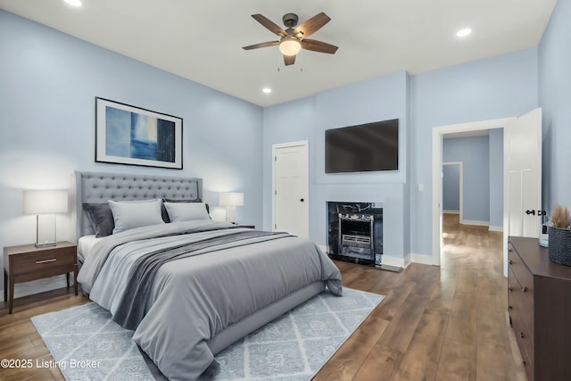 bedroom with recessed lighting, a high end fireplace, ceiling fan, wood finished floors, and baseboards