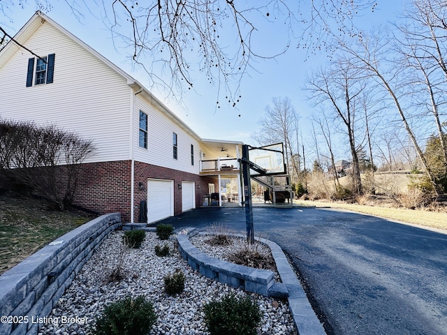 view of home's exterior featuring a garage, stairs, aphalt driveway, and brick siding