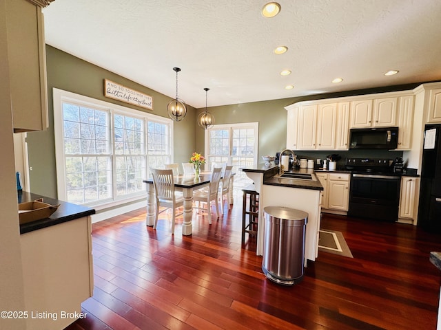 kitchen with a sink, dark wood-style floors, black appliances, dark countertops, and a kitchen bar