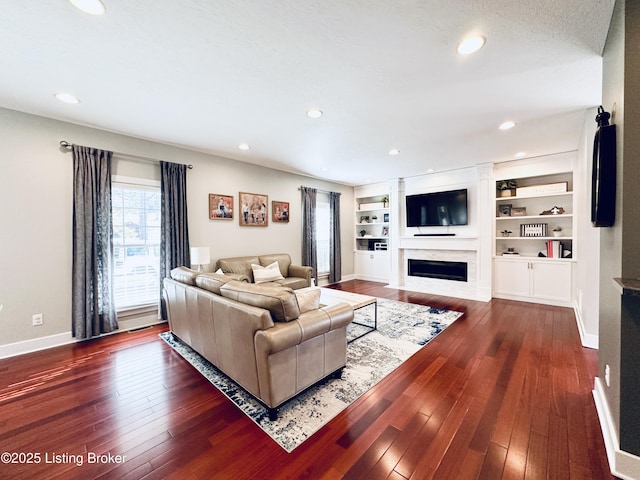 living room featuring hardwood / wood-style flooring, recessed lighting, built in features, baseboards, and a glass covered fireplace