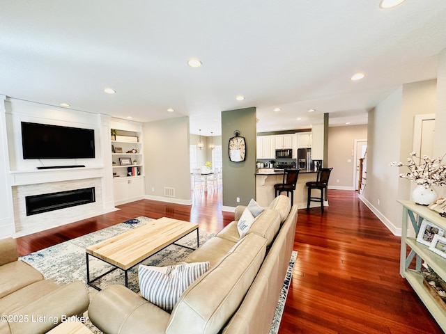 living area with built in shelves, dark wood-style flooring, recessed lighting, a premium fireplace, and baseboards