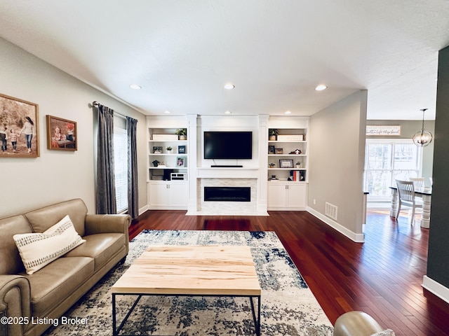 living room with a fireplace with flush hearth, visible vents, built in features, baseboards, and dark wood finished floors