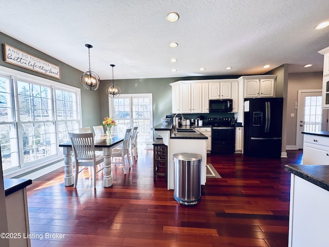 kitchen with dark countertops, white cabinets, a sink, a peninsula, and black appliances